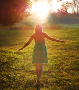 Woman walking with hands out in a field into the sunset