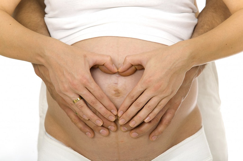 Man and women's hands in the shape of a heart over lady's pregnant belly.
